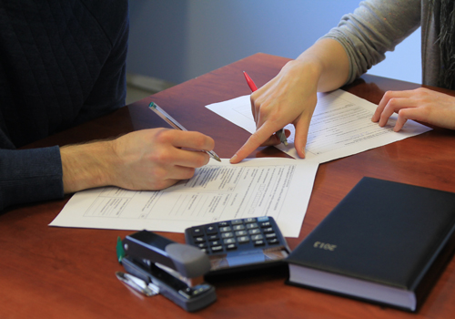 Twee personen zitten aan een tafel en vullen samen een document in.