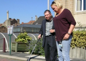 Een begeleidster van de Brailleliga leert een blinde persoon verplaatsingstechnieken aan.