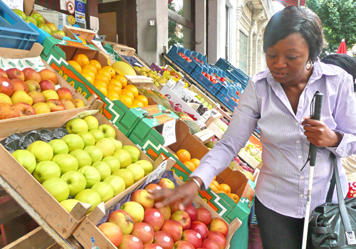 Une personne aveugle touche des pommes sur un marché.