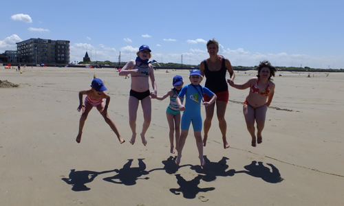 Des enfants sautent en l’air sur la plage.