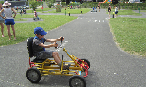 Un jeune déficient visuel conduit un cuistax sur un parc automobile.