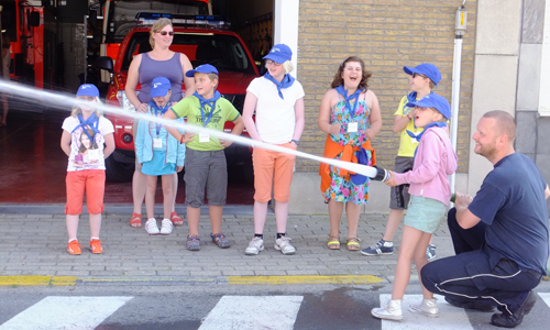 De kinderen leren een brandweerslang te gebruiken.