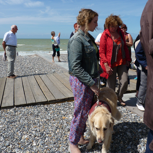 Une jeune déficiente visuelle et son chien-guide sur la plage de galets bleus.