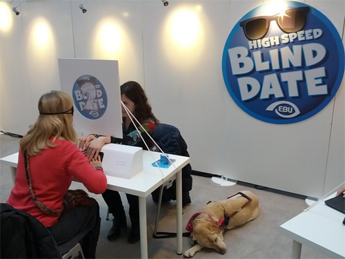  Een parlementslid op de stand van de Blind Date actie laat zich leiden door een persoon met een visuele beperking die lid is van de European Blind Union.