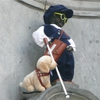 Manneken Pis habillé en Louis Braille, avec des lunettes noires, une canne blanche de locomotion et un chien-guide en peluche.