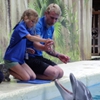 Kinderen met een visuele beperking strelen dolfijnen tijdens een stage aan zee.