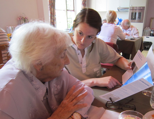 Een vrouw bladert samen met een oudere vrouw door een brochure van de Brailleliga in woonzorgcentrum 