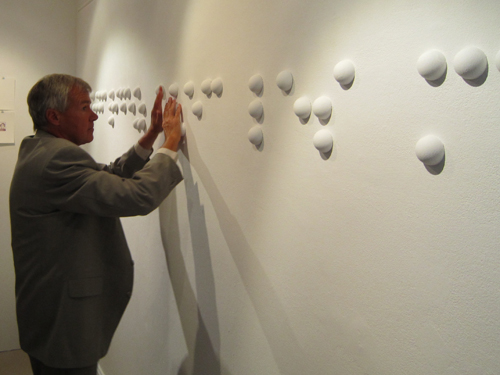 Une personne aveugle lit du braille apposé sur un mur de l’exposition du Musée Ianchelevici.