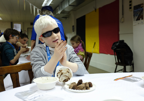 Un enfant déficient visuel portant des lunettes roule du chocolat entre ses mains pour en faire une truffe.