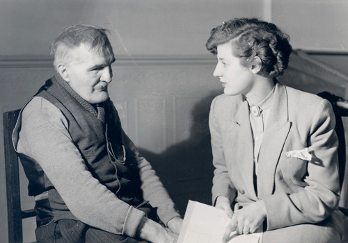 Image d'archive d'une assistante sociale assise aux côtés d'une personne aveugle âgée
