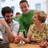 Deux personnes déficientes visuelles souriantes testent l’Apple Watch avec un vendeur d’Apple.