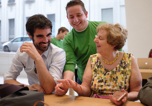 Twee mensen met een visuele handicap testen samen met een verkoper de Apple watch. Alle drie lachen ze. 