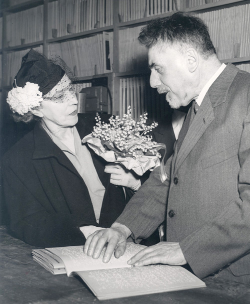 Image d'archive de la reine Elisabeth en visite à la Ligue Braille. Elle se tient en compagnie de Gérard Borré (président de la Ligue Braille à ce moment) dont les mains sont posées sur un livre braille