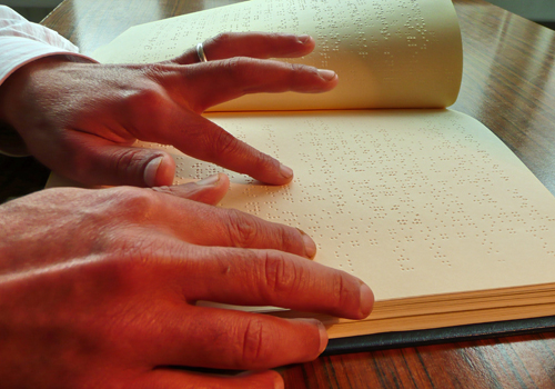 Mains d’une personne aveugle occupée à lire un document en braille.