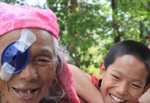 Un enfant et une personne âgée sourient. La personne âgée a un cache-oeil sur son oeil droit.