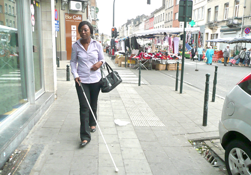 Une personne déficiente visuelle marche en rue à l'aide d'une canne blanche