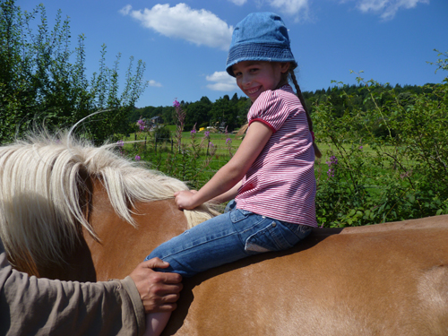 Un enfant déficient visuel se balade à dos de poney accompagné du guide.