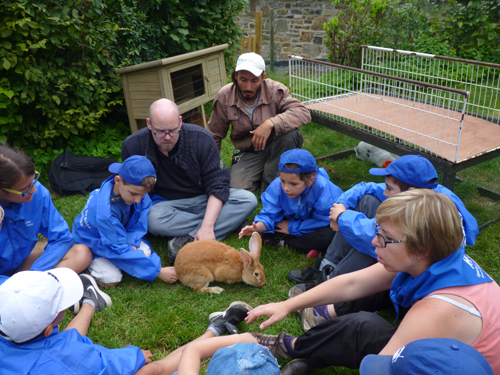 Les enfants sont assis en rond et caressent les lapins de la ferme.