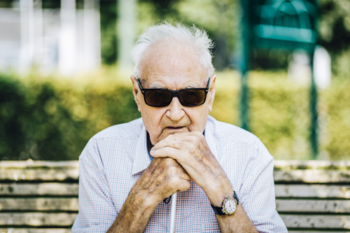 Une personne malvoyante assise sur un banc tout en tenant sa canne blanche