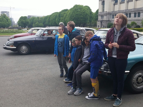 Een groep kinderen wacht bij enkele oldtimers. 