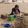 Un garçon construit un château de sable sur la plage.