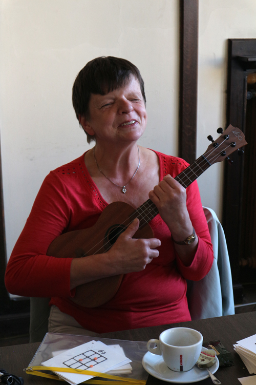 Een deelneemster zit aan tafel met een ukelele in de hand en is aan het lachen. 