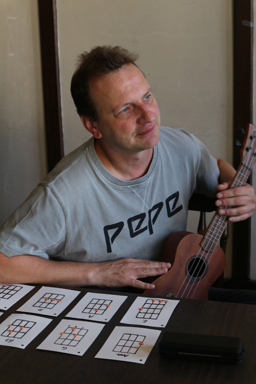 Een deelnemer zit aan tafel met een ukelele in zijn linkerhand. Voor hem liggen tactiele kaarten. 