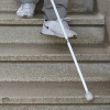 Une déficience visuelle descend un escalier avec l’aide de la canne blanche.