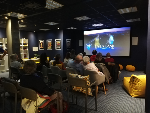 plusieurs personnes installées sur des chaises devant l’écran de cinéma dans la salle BrailleMedia