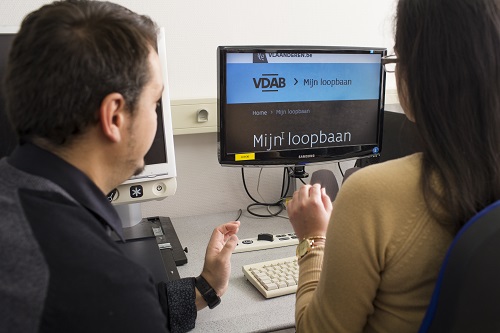 Een medewerker van de Brailleliga kijkt toe hoe een vrouw met een visuele handicap de website van VDAB bezoekt. 