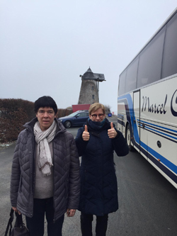 Twee personen naast een bus met op de achtergrond een windmolen.