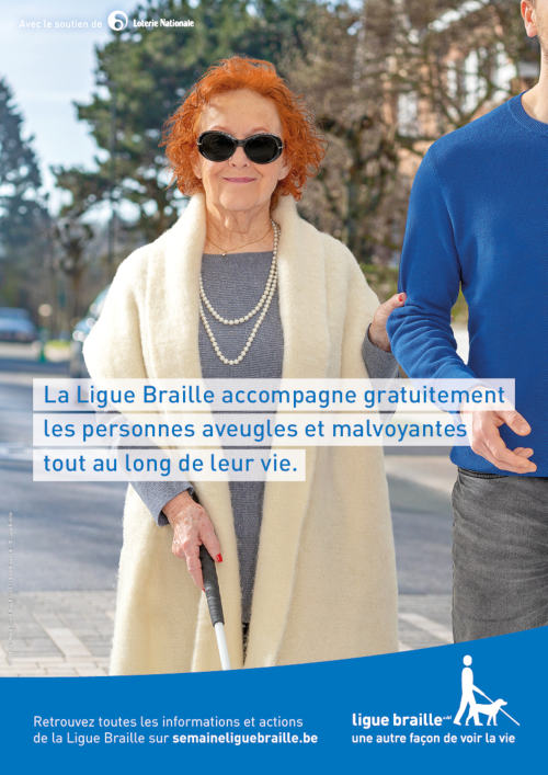 Une dame âgée et aveugle se fait tenir le bras par un homme en pull bleu