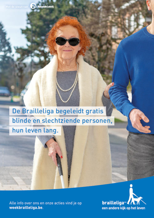 Een bejaarde blinde dame die door een man in blauwe trui begeleigd is