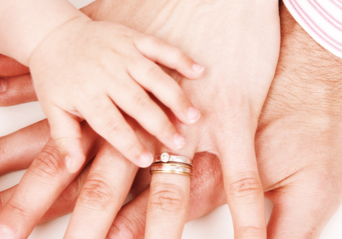 Handen van een pasgeborene, met daarbovenop de hand van een vrouw en een man.