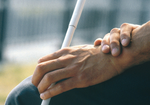 Handen van een blinde persoon die een witte stok vasthouden