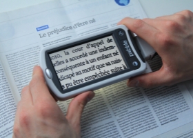 Une personne malvoyante utilise une loupe électronique pour lire son journal