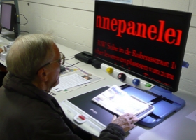Ein älterer Mensch testet eine Videolupe auf der BrailleTech-Messe.