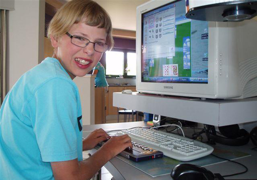 Eine junge sehbehinderte Person bei der Arbeit mit ihrem angepassten Computer.