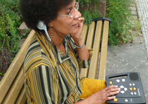 Eine Person sitzt auf einer Bank und lauscht einem Hörbuch mithilfe eines Daisy-Abspielgeräts.