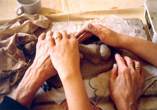 A volunteer helping a visually impaired person handle clay as part of a BrailleClub activity.